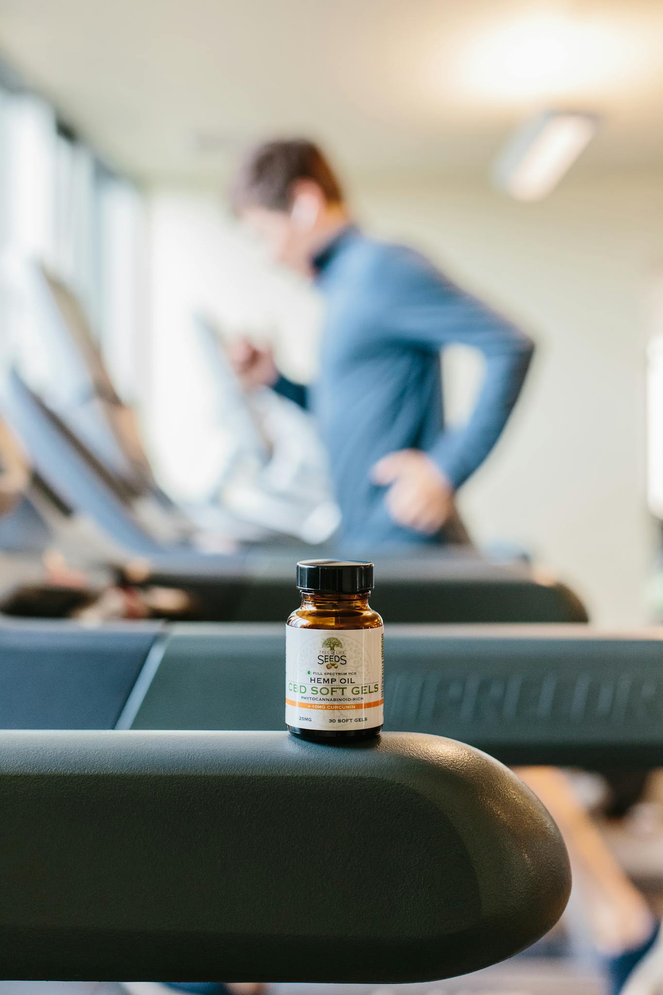 Supplement bottle in focus on treadmill with blurred male runner exercising in background.